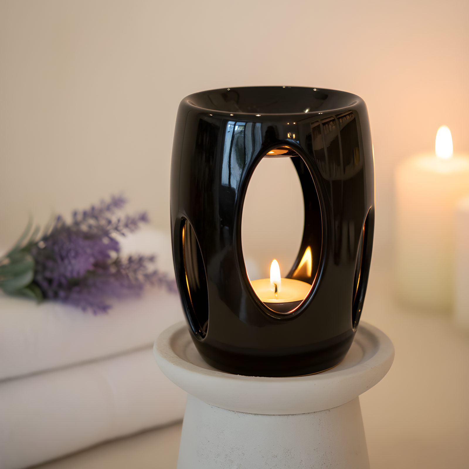 Black ceramic wax melt burner with a lit candle inside on a white surface, with a blurred background.